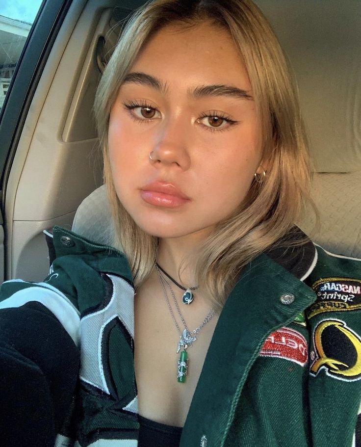 a woman sitting in the back seat of a car wearing a green jacket and necklace