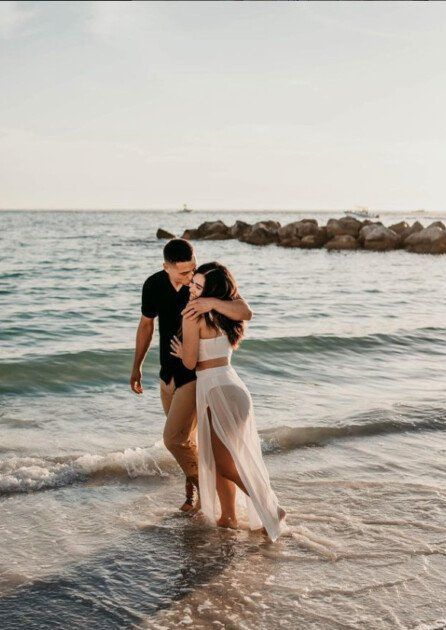 two people standing in the water at the beach with their arms around each other as they hug