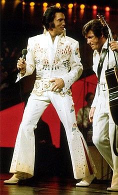 two men dressed in elvis style clothing, one holding a guitar and the other singing