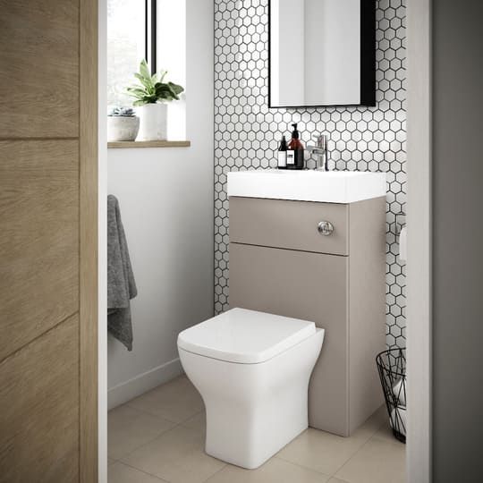 a white toilet sitting under a bathroom mirror next to a sink in a room with tiled walls