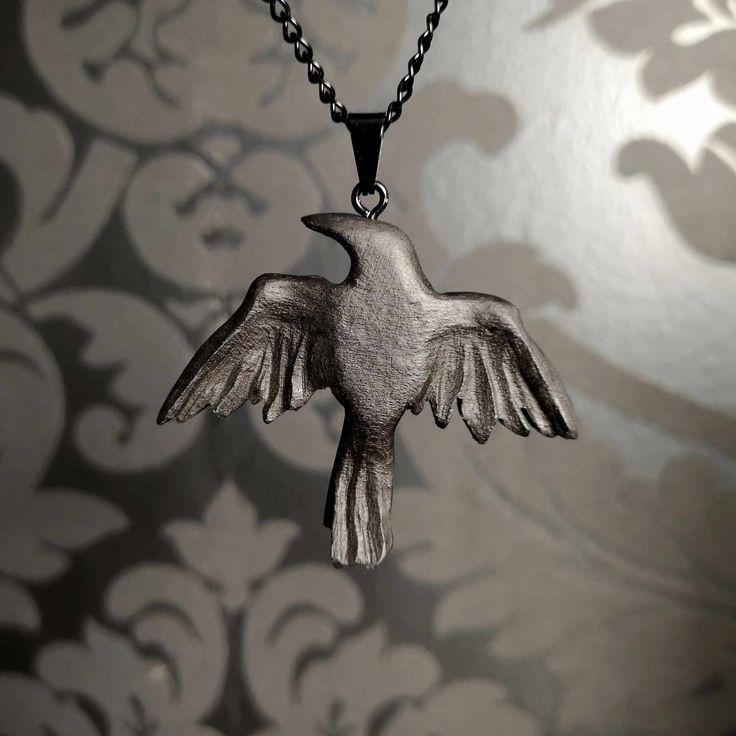 a silver bird necklace on a chain with an intricate pattern in the wall behind it