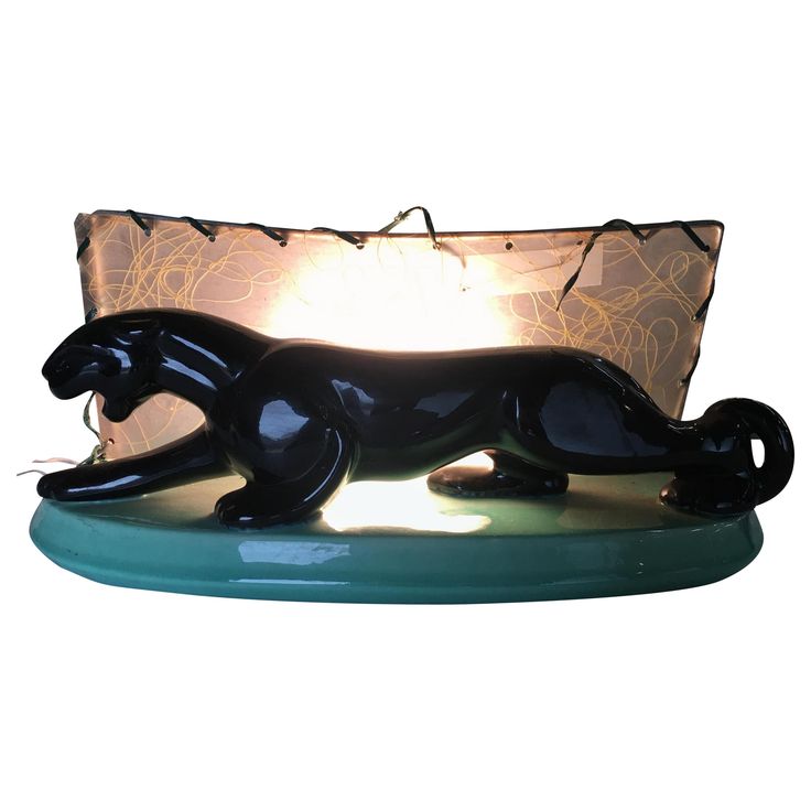 a black cat figurine sitting on top of a green table next to a lamp