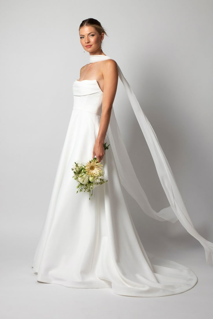 a woman in a white wedding dress holding a bouquet and a veil over her head