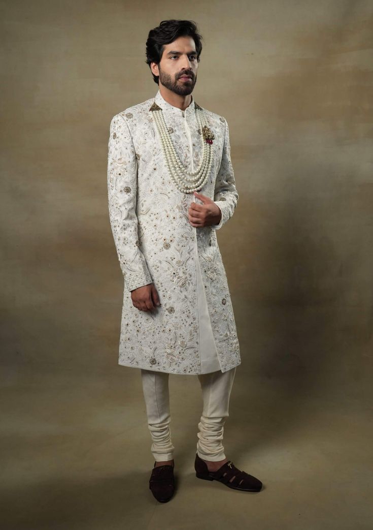 Editor's Note Featuring our work of art in our white all over hand-embroidered sherwani set. The foundation is crafted using machine embroidery adorned with tone on tone thread serving as the base texture, while the second tier showcases highlighting with 3D brass elements, dabka and zari threads. Fabric: Linen silk Color: Ivory, gold Components: Sherwani, kurta and churidar Occasion: Groom Fit: Regular Note: Product colour may slightly vary due to photographic lighting sources Care: Dry clean o Designer Off-white Bandhgala With Resham Embroidery, Designer Off-white Traditional Wear With Chikankari Embroidery, Designer Off White Traditional Wear With Chikankari Embroidery, Formal White Raw Silk Traditional Wear, Designer Off White Festive Sets, Gold Raw Silk Sherwani With Chikankari Embroidery, Designer Unstitched White Kurta, Designer White Unstitched Kurta, Ceremonial Cream Raw Silk Sherwani