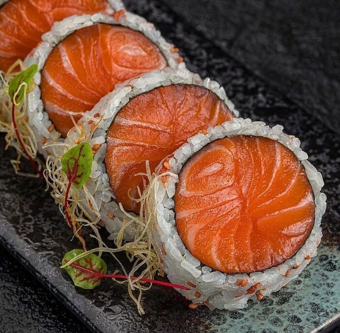 three sushi rolls on a black plate with sprouts and seaweed in the middle