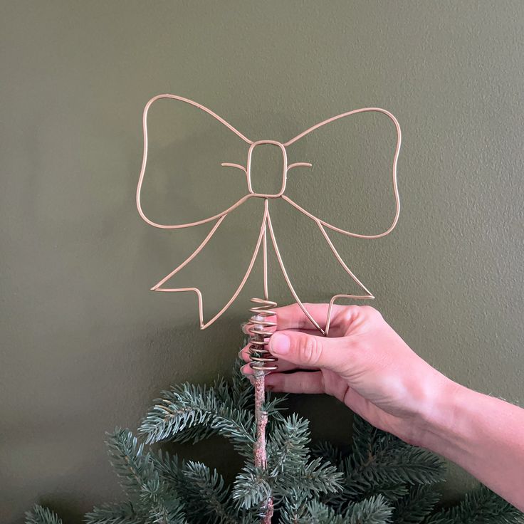 a hand holding a wire bow on top of a christmas tree