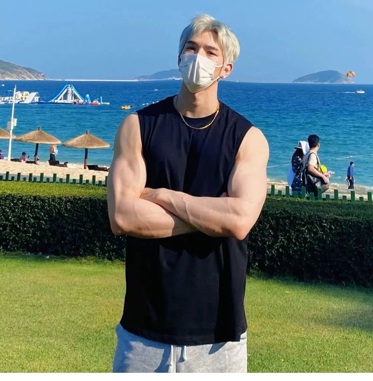 a man wearing a face mask standing in front of the ocean with his arms crossed