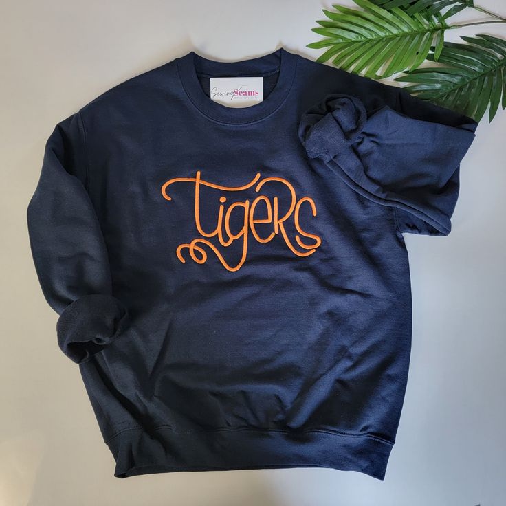 Are you a devoted fan of Auburn University's Tigers? Do you bleed orange and blue for your team? Then, this Tigers sweatshirt is tailor-made for you! Show your unwavering support for the Tigers in style and comfort with our exclusive Auburn Tigers sweatshirt.Product Details:🔵 Striking Navy Blue Color: Our Tigers sweatshirt comes in a bold navy blue hue that's as captivating as the Auburn Tigers' performance on the field. This color is sure to make you stand out in the crowd and represent your t Personalized Slippers, Navy Blue Sweatshirt, Graduation Stole, Baby Beanie Hats, College Shirts, Baby Bloomers, Auburn University, Auburn Tigers, Embroidered Clothes