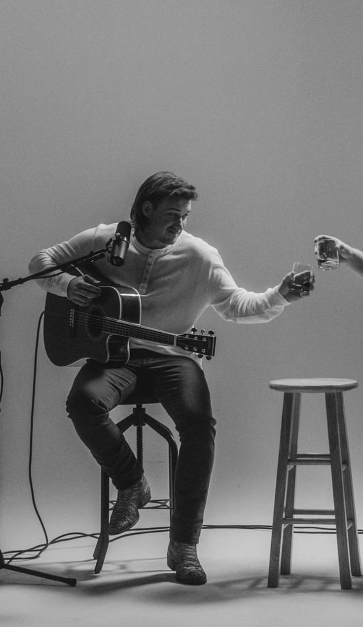 two people sitting in chairs playing guitar and singing into microphones while another person sits on stool