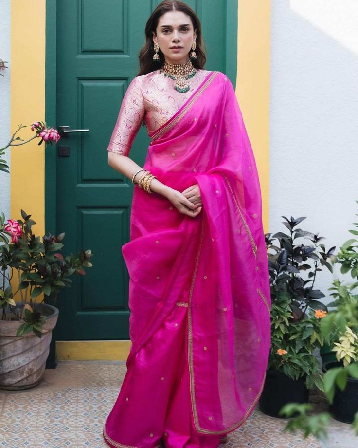 a woman standing in front of a green door wearing a pink sari