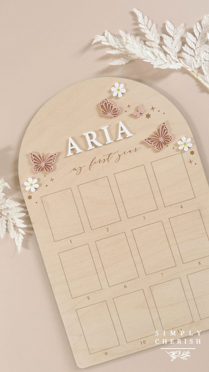 a wooden calendar with butterflies and flowers on it, next to some white leaves in the background