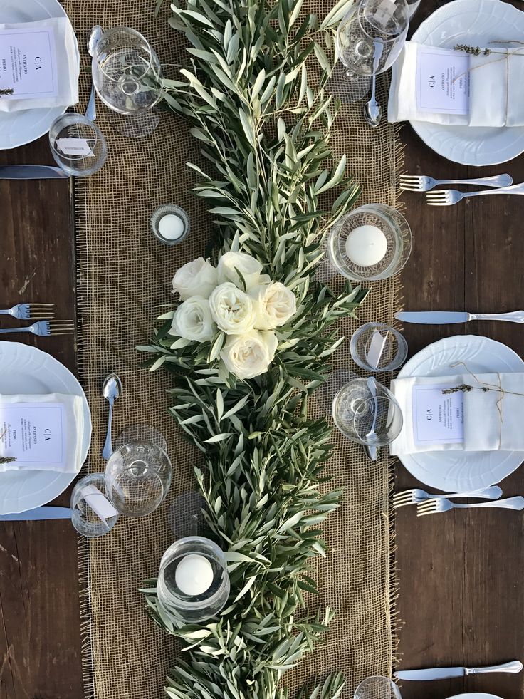 an arrangement of white flowers and greenery on a burlocked table runner