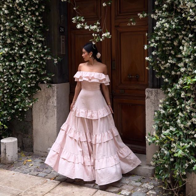 a woman standing in front of a door wearing a pink dress with tiered ruffles