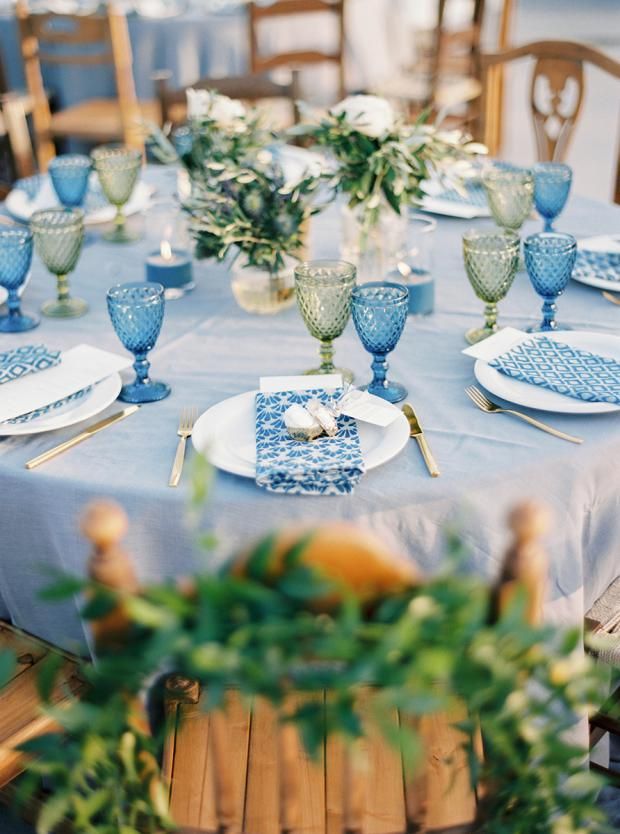 the table is set with blue and white plates, silverware, and greenery