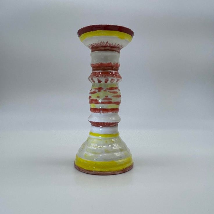 a yellow and red glass vase sitting on top of a white tablecloth covered floor