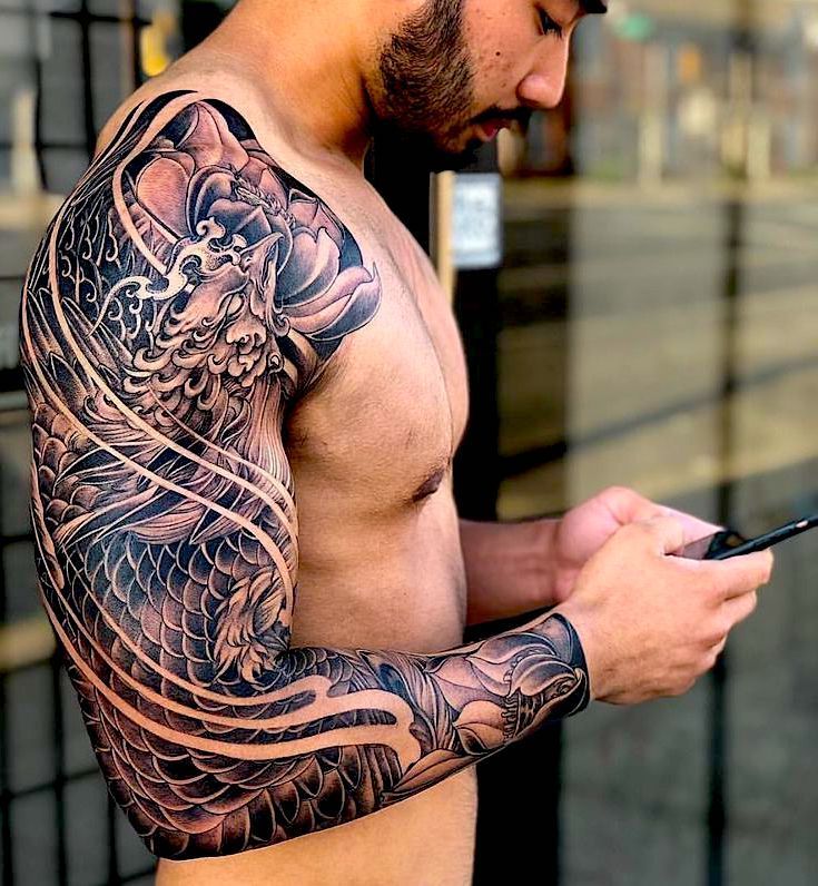 a man with a dragon tattoo on his arm holding a cell phone and looking at it