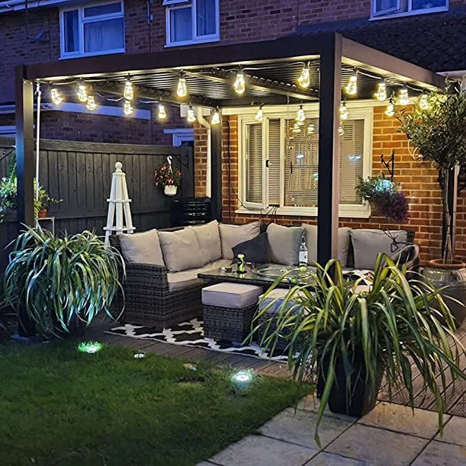 an outdoor living area is lit up at night with lights on the roof and potted plants