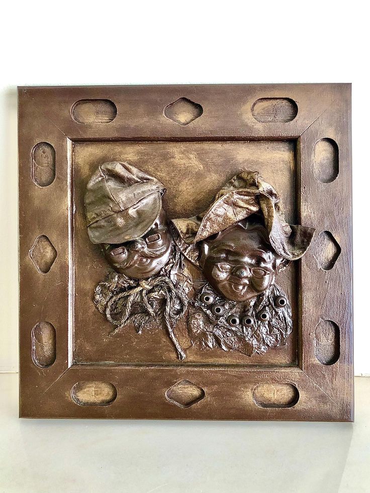 a bronze sculpture of two men with hats and beards in a square metal frame