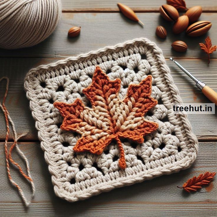 a crocheted square with an orange maple leaf on it next to yarn and nuts