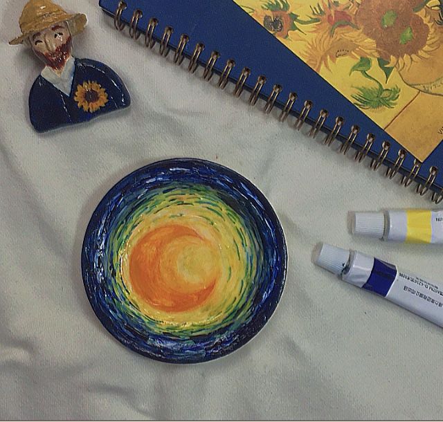 a spiral notebook and some markers are on a table next to a plate with an image of a clown