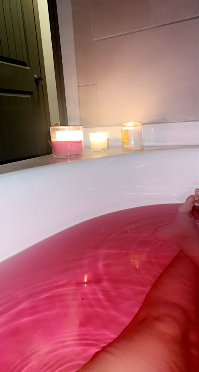 two candles sitting on top of a bathtub filled with pink liquid