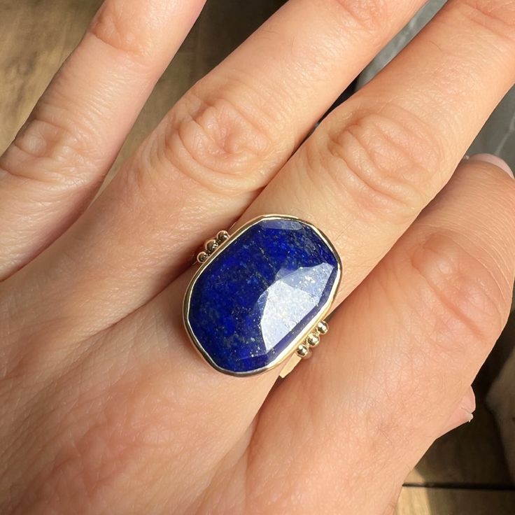 We love this cocktail Lapis ring set in 14k yellow gold. It is accented with gold beads and sits beautifully on Emily's signature Sterling Silver band. Approximate stone size is 20mm x 14mm. Approx ct weight: 10.6 ct Mohs hardness: 5-6 This mixed metal piece is handmade to order in Emily's Hudson Valley studio. Please allow for slight variations in stone color, size and shape. Please allow 14-21 days to ship unless the piece is in stock. If you have questions about sizing, shipping or custom ord Unique Faceted Yellow Gold Ring, 14k Yellow Gold Jewelry With Natural Stones, 14k Gold Jewelry With Natural Stones, Heirloom Faceted Gold Jewelry, Sterling Silver Gold Rings With Gemstone, 14k Gold Gemstones With Gemstone Accents, 14k Gold Jewelry With Large Stone Ring, Gold Sterling Silver Rings With Gemstone, Gold Gemstones Ring With Gemstone Accents