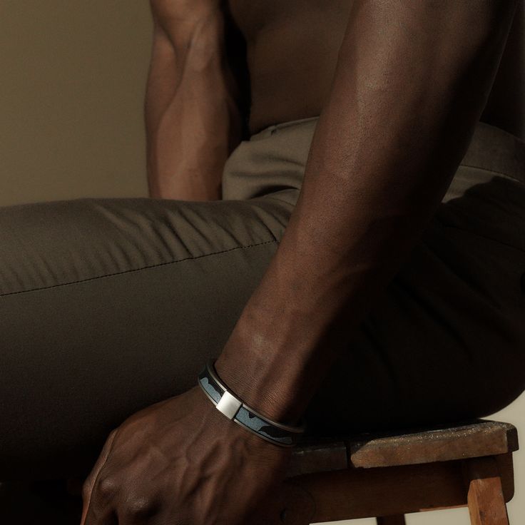 a man sitting on top of a wooden stool wearing a silver bracelet and brown pants