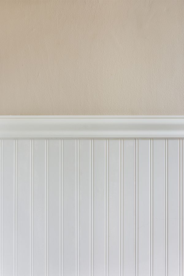 a cat sitting on top of a wooden bench in front of a white paneled wall