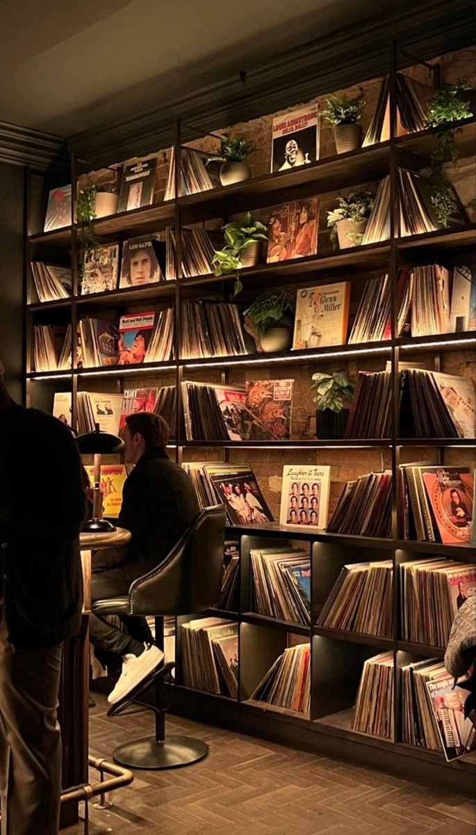 people are sitting at tables in front of a book shelf filled with records and cds