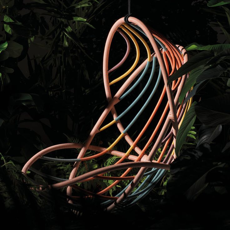 an abstract sculpture made out of colored wires in the dark forest with green leaves around it