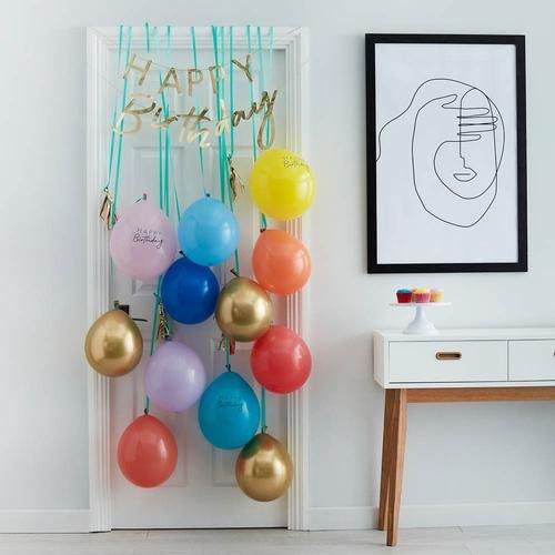 balloons and streamers are hanging on the wall near a table with a white dresser