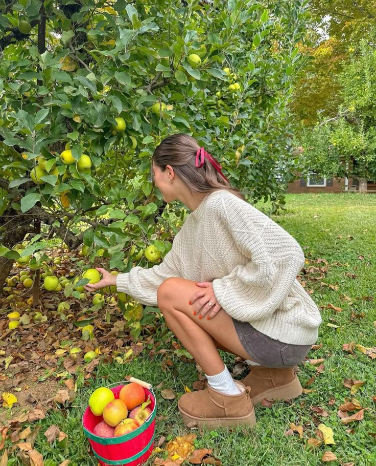 a woman kneeling down to pick apples from a tree