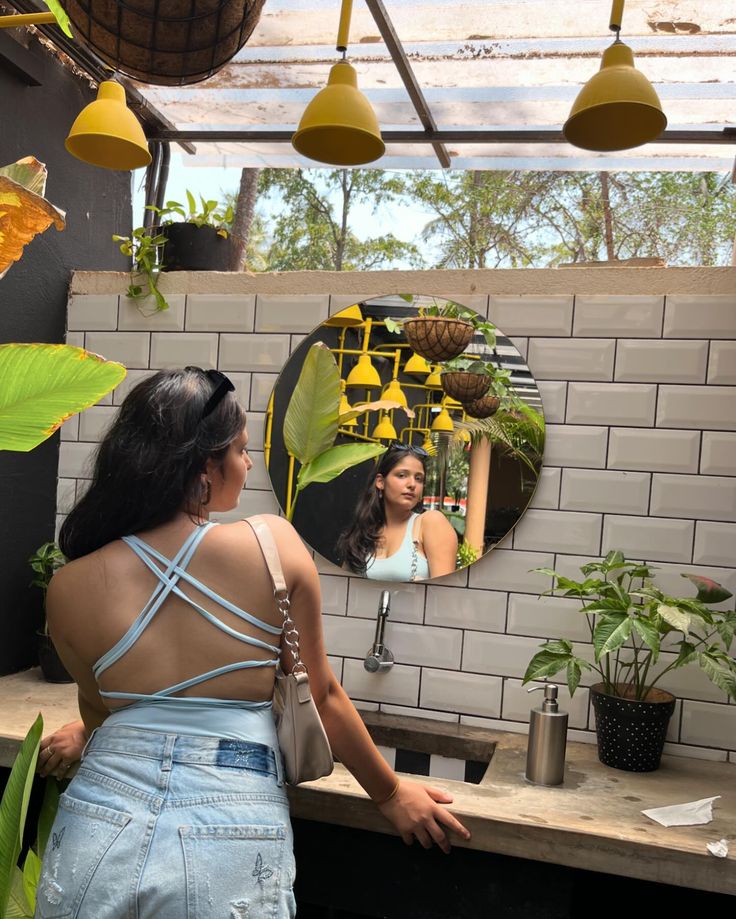 a woman standing in front of a mirror next to plants and potted plants on a counter