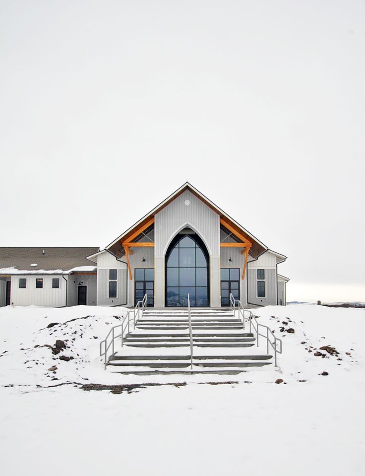 a church in the snow with stairs leading up to it's door and windows