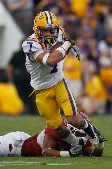 a football player running with the ball in his hand and another person laying on the ground behind him