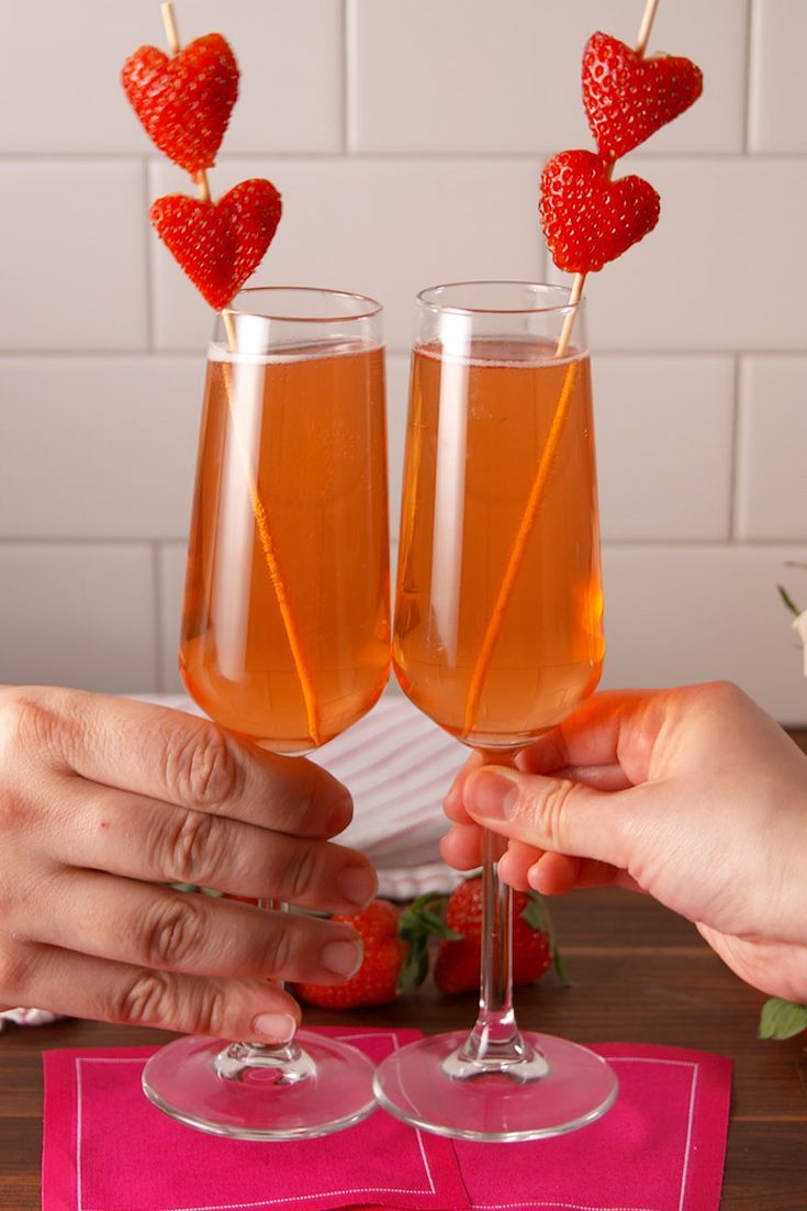 two people holding wine glasses with strawberries on them