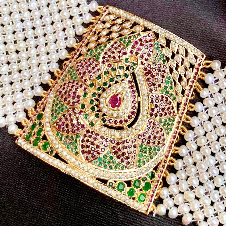 Traditional punjabi jadau bracelet called "Baahi" in 92.5 gold plated silver. All pearls used are freshwater pearls. The stones. in setting are synthetic rubies and emeralds of high quality. Weight 43 GMs Height 5.5 cm Length 15 cm All of Rudradhan's Gold Plated Jewellery is made using 925 Silver, real freshwater pearls and high quality ruby, emerald and sapphire beads. The default choice for studded stones used is synthetic that closely resemble original gemstones. Traditional Pearl Bracelet For Festive Occasion, Traditional Festive Pearl Bracelet, Festive Pearl Bracelet For Gift, Festive Pearl Bracelet Perfect For Gifts, Traditional Gold Pearl Bracelet For Celebration, Traditional Pearl Bracelets For Gifts, Traditional Pearl Bracelets As A Gift, White Kundan Temple Jewelry Bracelets, Traditional Ruby Bracelets For Festive Occasions