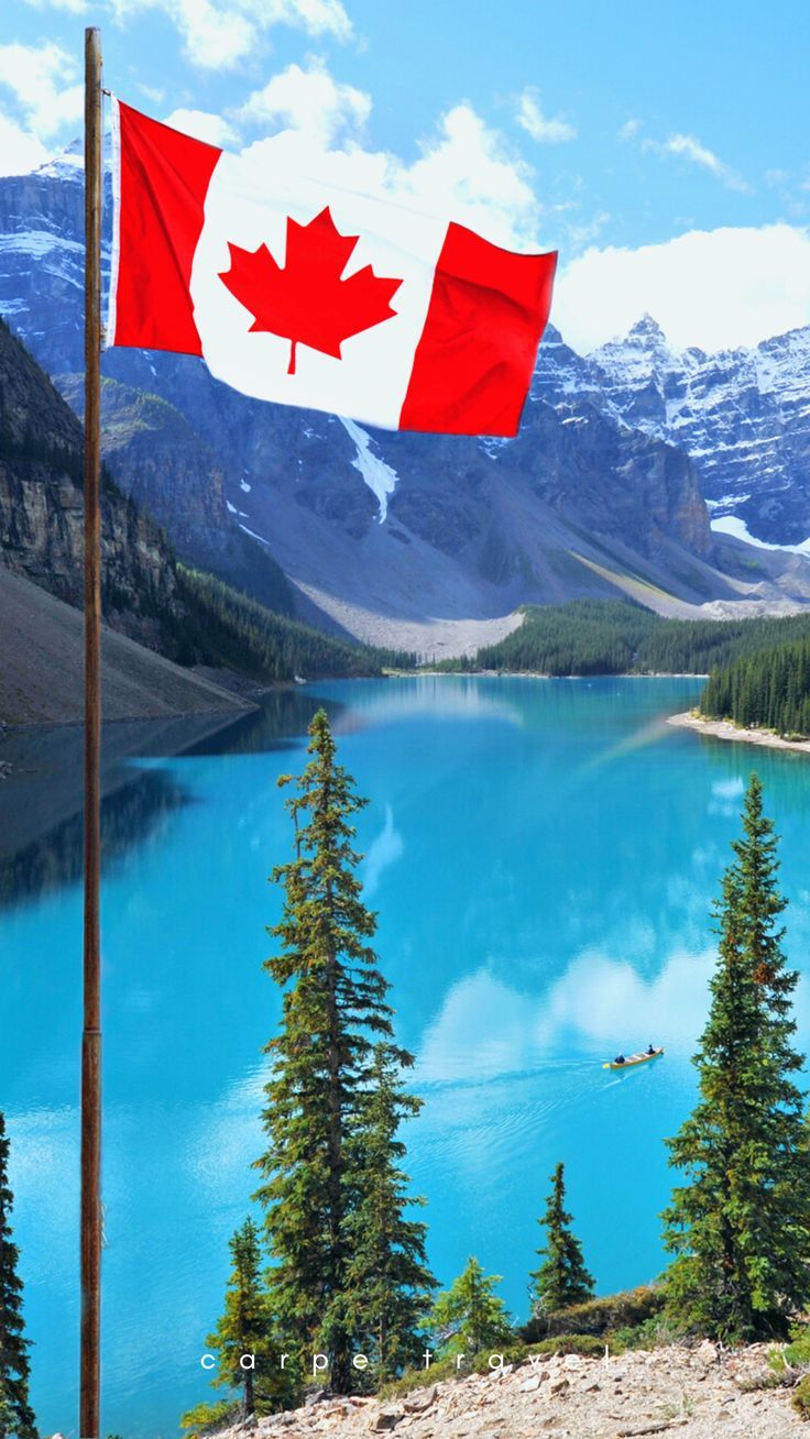 a canadian flag flying over a lake surrounded by mountains