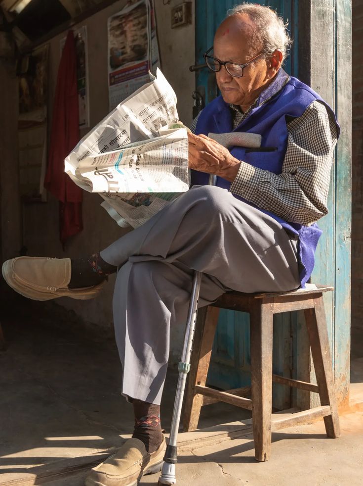 an old man sitting on a chair reading a newspaper