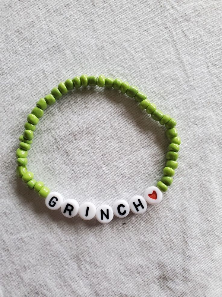 a green beaded bracelet with the word grin written in white letters on it and a red heart