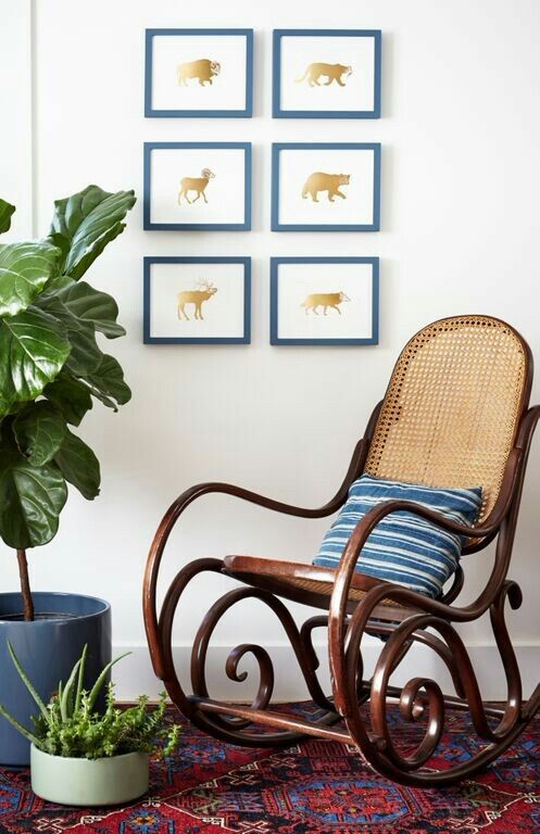 a rocking chair next to a potted plant and pictures on the wall