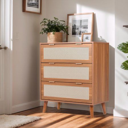 a wooden dresser sitting next to a door with pictures on top of it and a potted plant in the corner