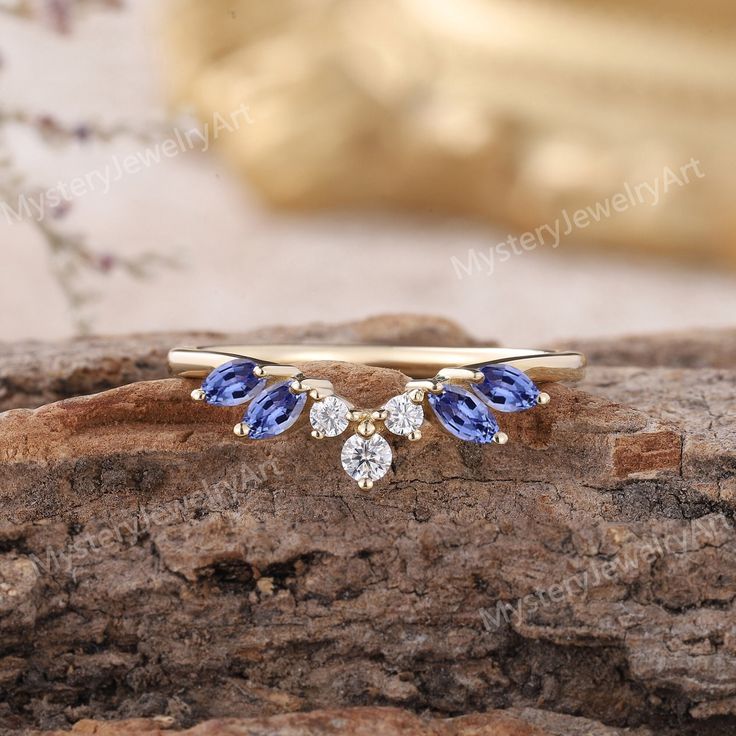 a gold ring with two blue and white stones on it, sitting on top of a piece of wood