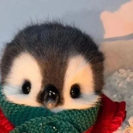 a stuffed animal penguin wearing a green and red scarf with snow around it's neck