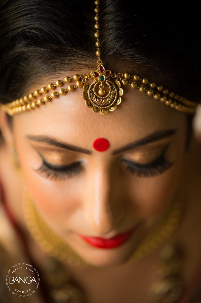 a woman wearing a gold head piece and red nose ring, with her eyes closed