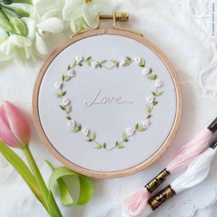 a cross stitch heart with the word love in it surrounded by flowers and two crochet hooks