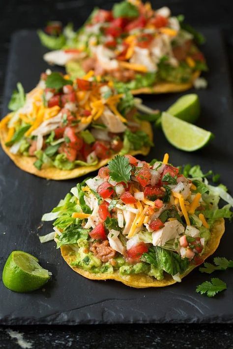 three tacos with chicken, lettuce and salsa on them sitting on a table