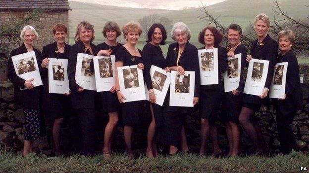 a group of women standing next to each other holding framed pictures in front of a stone wall