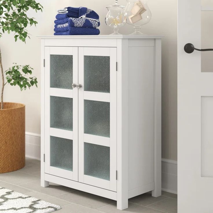 a white cabinet sitting next to a potted plant and glass door with towels on top