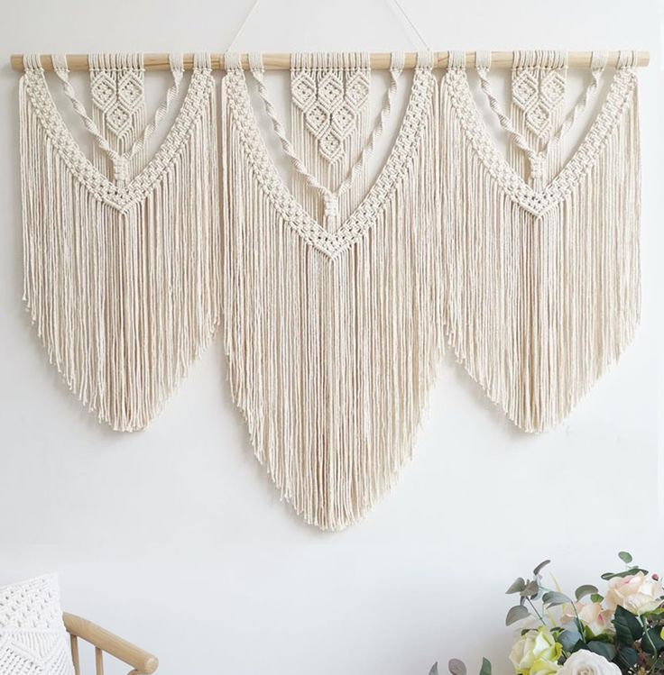 three macrame wall hangings with white flowers in the foreground and a wooden chair on the other side